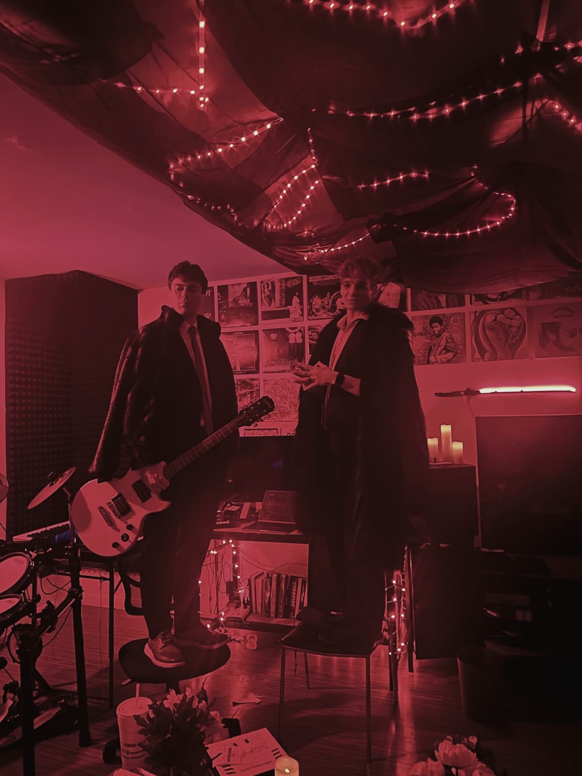 The whole studio flooded red: record wall, canopy lights, a guitarist and a friend in long coats